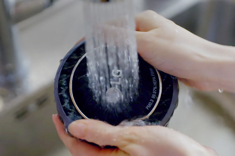 تمسك يد المرأة بجوانب المرشح بينما يتم غسله بالماء تحت صنبور جارٍ.