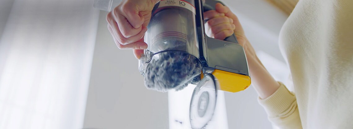 تقبض المرأة على مقبض المكنسة الكهربائية وتستخدم اليد الأخرى لتحريك الرافعة لإفراغ العلبة بسهولة.