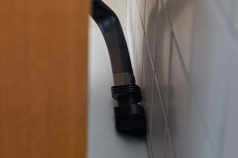 تظهر أداة الشقوق المرنة خلف قطعة أثاث لإزالة الغبار والأوساخ بين الأثاث والحائط.