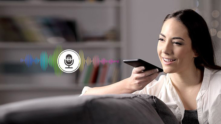 امرأة تتحكم في التلفزيون من خلال التحدث إلى جهاز تحكم عن بعد به خاصية التعرف على الصوت.	