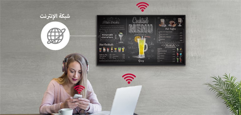 صورة توضح شاشة من سلسلة UR3J معلقة على الجدار وامرأة تستخدم جهاز حاسوب شخصي وهاتف محمول. تشير هذه الصورة أنه يمكن توصيل اللافتات لاسلكيًا بجهاز الحاسوب والهاتف المحمول الذي تحمله المرأة.