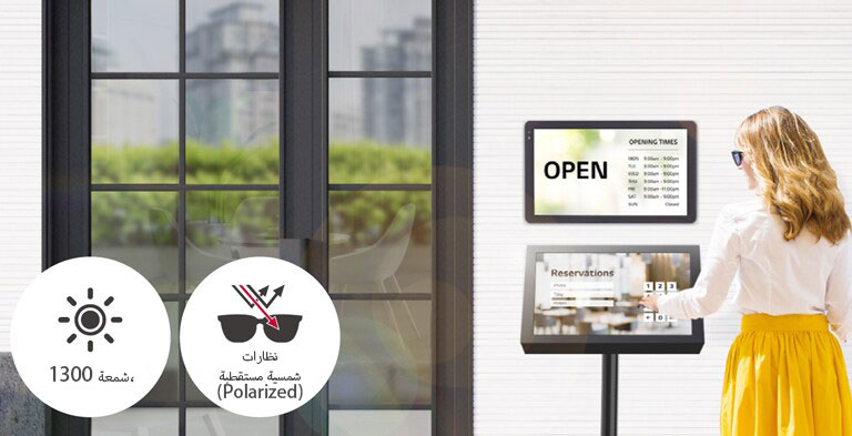 تم تركيب 22XF1TJ على الحائط عند مدخل المبنى مع حامل 22XF1TJ آخر بالأسفل لأغراض الحجز. تستخدم السيدة التي ترتدي نظارات شمسية شاشة اللمس لإجراء حجز. تظل الشاشة مرئية حتى عندما تكون تحت أشعة الشمس المباشرة.