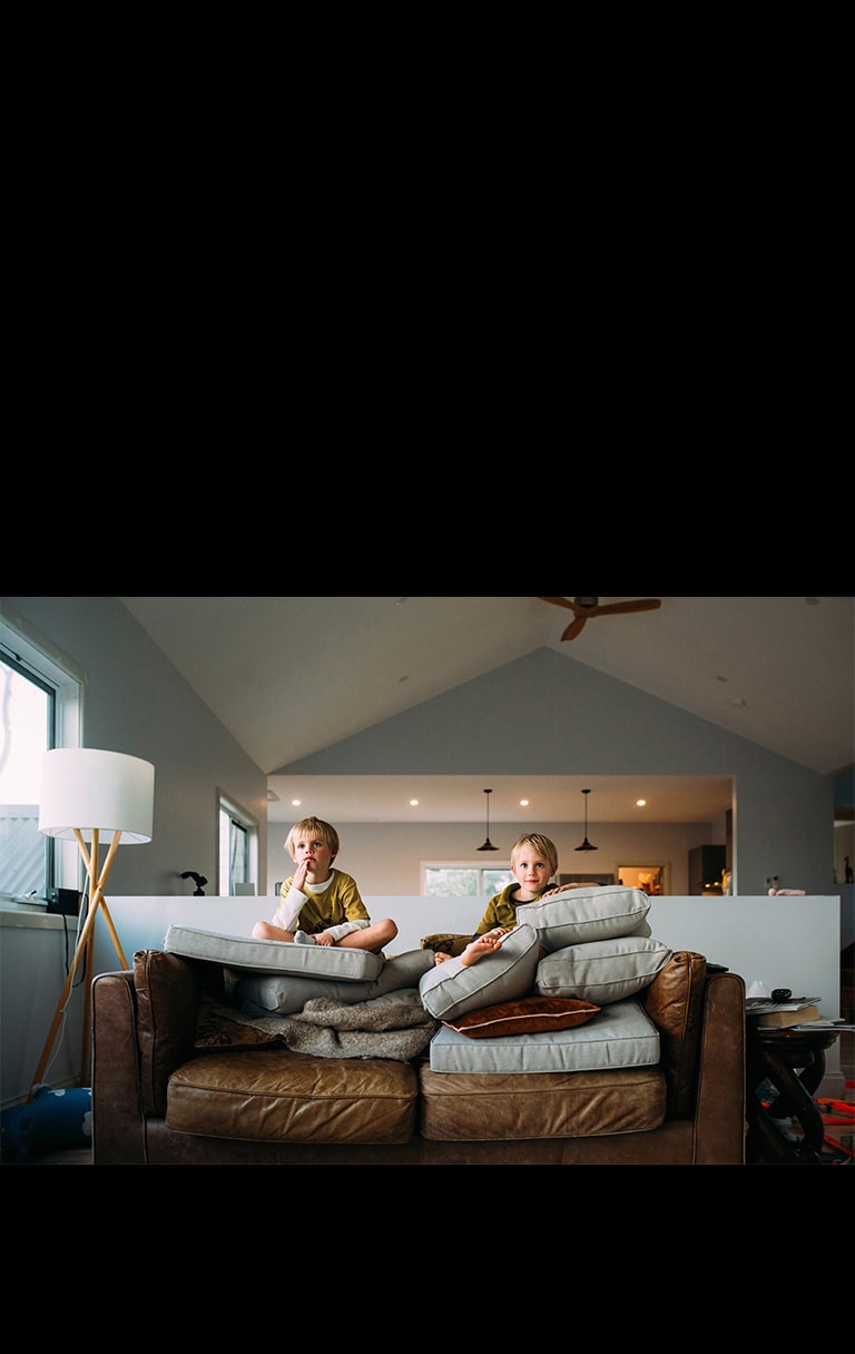 صبيان توأمان يشاهدان شيئًا أثناء جلوسهما على الأريكة.