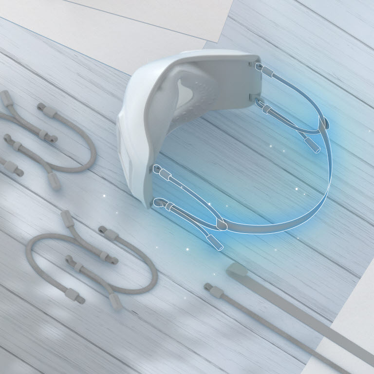 يظهر الجزء العلوي والداخلي من القناع مع شريط قماش مرن متصل في الخلف ومظلل باللون الأزرق.  توجد شرائط قماش مرنة إضافية على الطاولة حول القناع. 