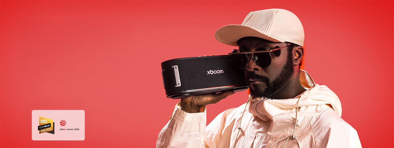 will.i.am يرتدي زيًا أبيض ونظارات شمسية ويمسك جهاز xboom Bounce بجانب وجهه مباشرةً.