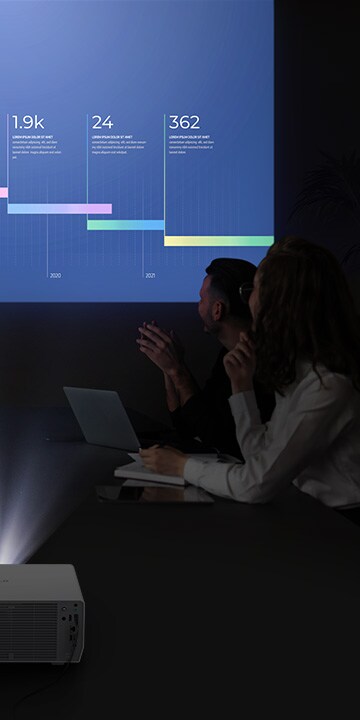 خمسة أشخاص يعقدون اجتماعًا في غرفة مظلمة، ويشاهدون شاشة نابضة بالحياة مع جهاز العرض LG ProBeam.