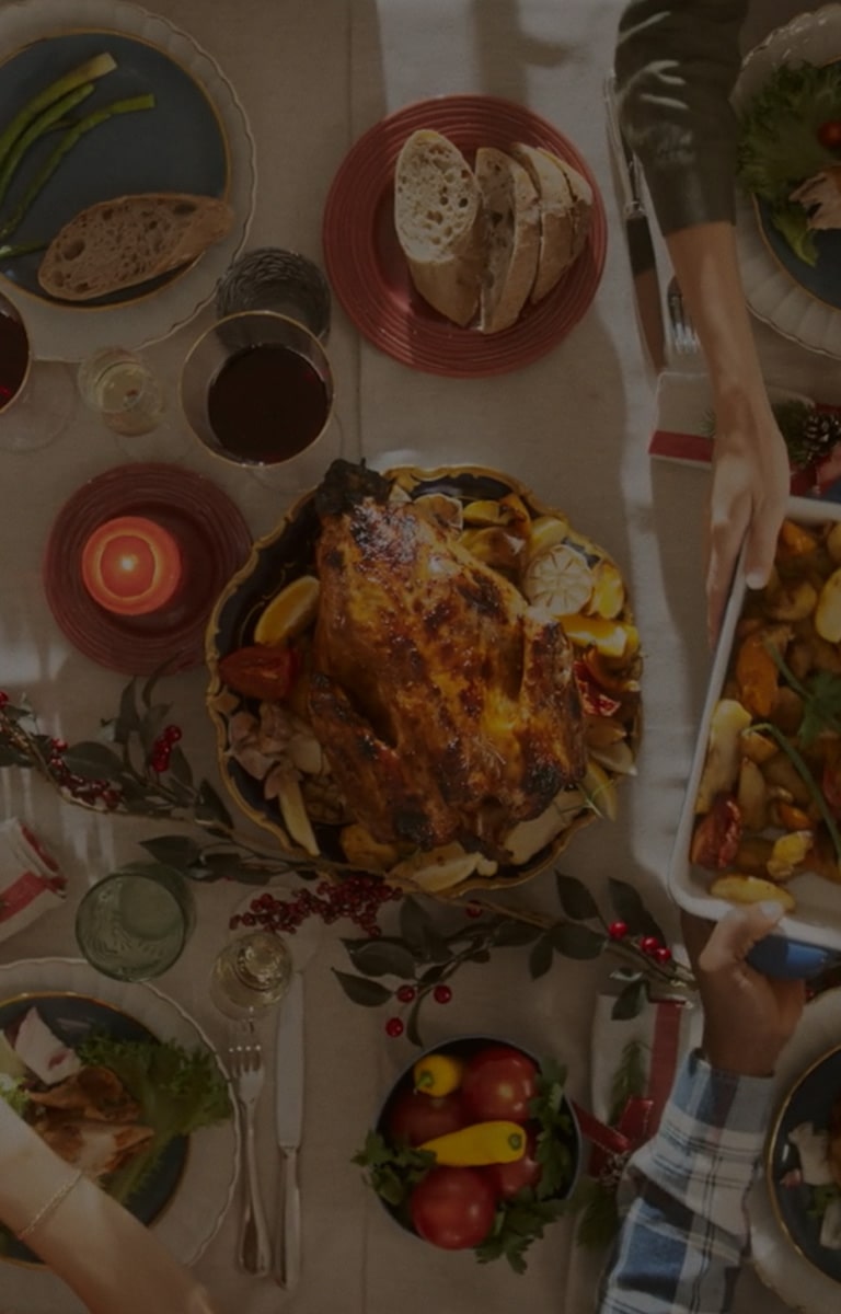 A dining table filled with various holiday dishes, fruits, and drinks, viewed from above, multiple hands are serving food.	