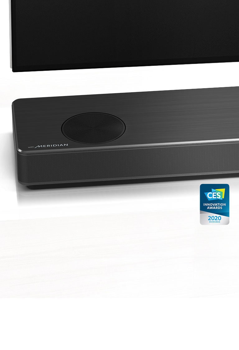 صورة مقرّبة توضح الجانب الأيسر من مكبر الصوت مع ظهور شعار ميريديان بالزاوية اليسرى السفلية للمنتج. يظهر بالصورة أيضًا الجانب الأيسر السفلي من التلفزيون.