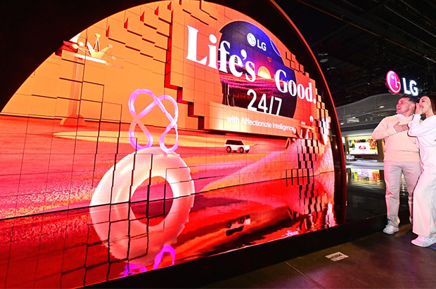 الزوار يشاهدون عرض شاشة LED المنحنية من LG التي تعرض شعار "الحياة جيدة على مدار الساعة طوال أيام الأسبوع" في معرض تكنولوجي.