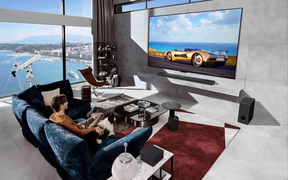A luxurious living room with a large LG TV displaying a car, a man on a sofa with a dog, and a stunning sea view.