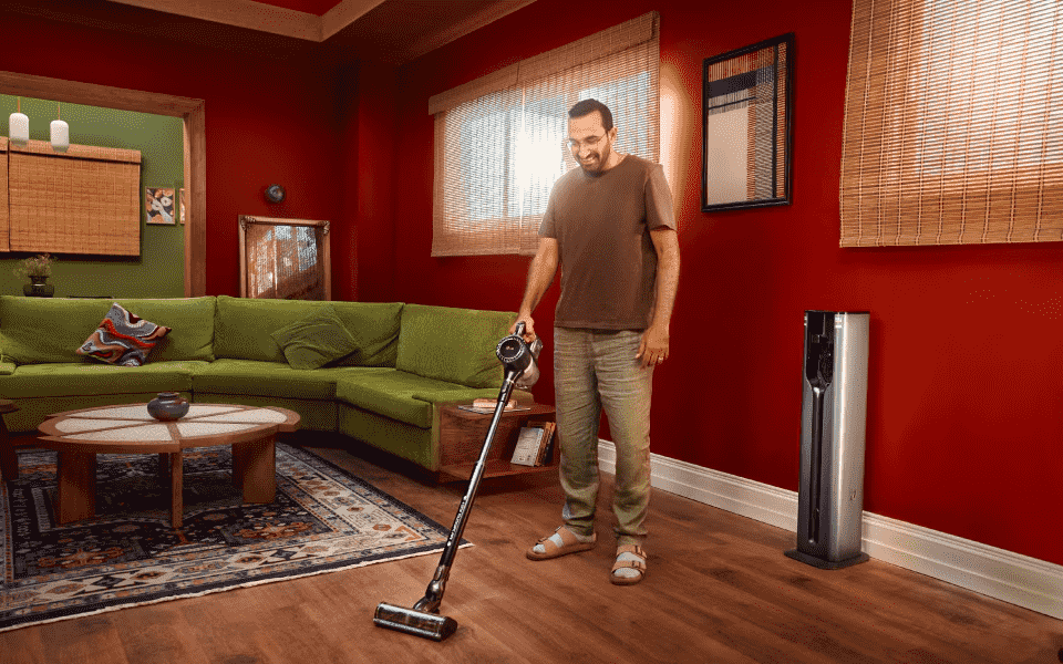Man happily vacuums with LG CordZero A9 Kompressor in a vibrant living room, showcasing effortless cleaning and modern design