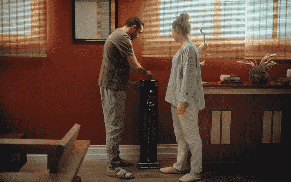 Couple assembling a black LG CordZero A9 Kompressor stick vacuum in a warm room. Demonstrates easy setup