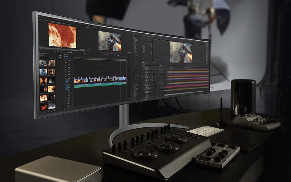A professional's LG UltraWide curved monitor displaying video editing software on a modern, high-end workstation
