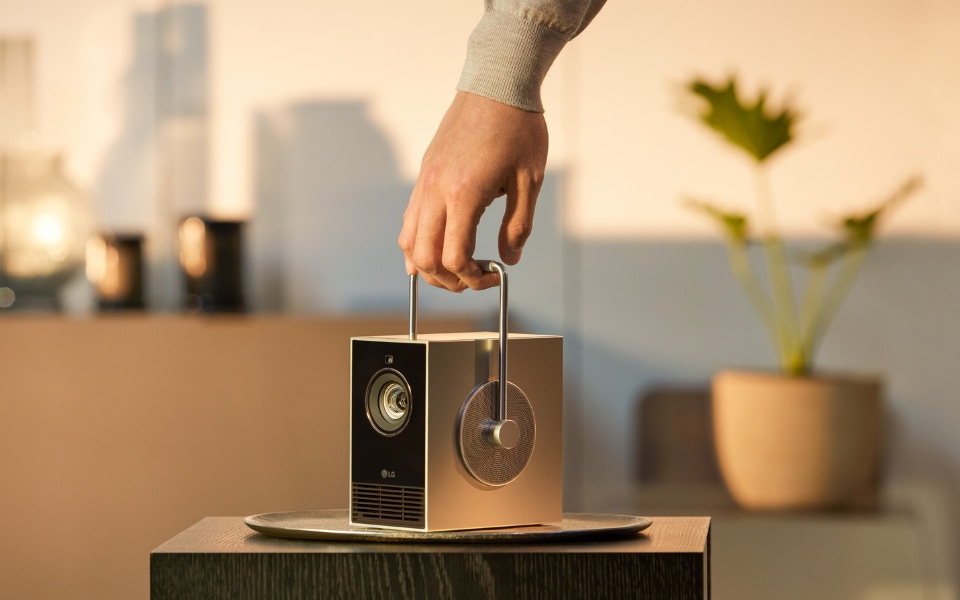Hand lifting a LG portable projector with sleek design, placed on a modern table indoors.