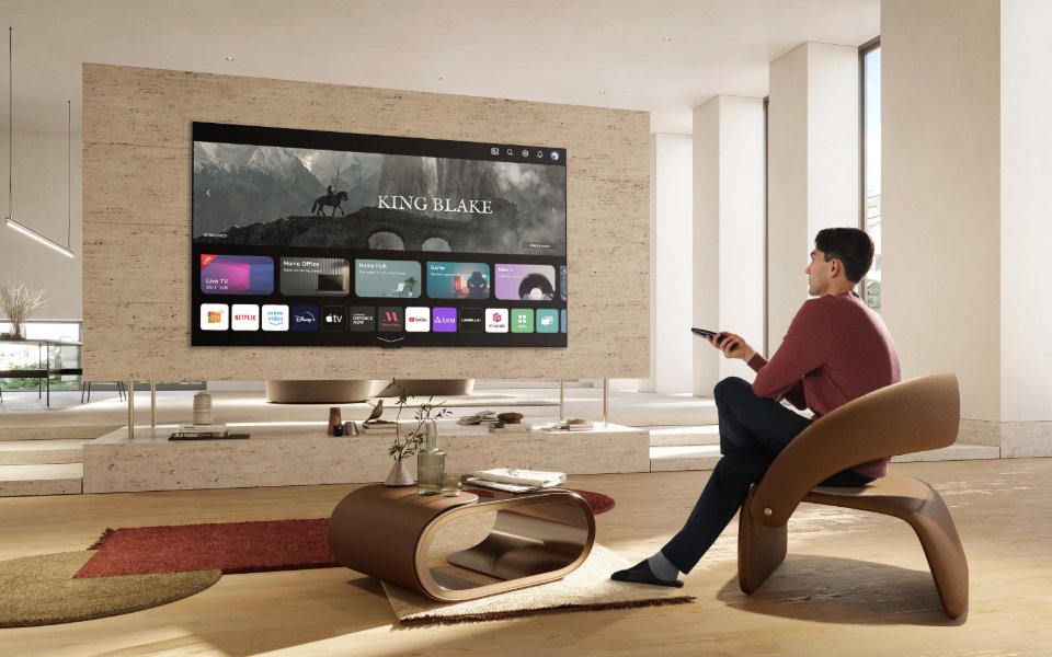 يجلس رجل في غرفة معيشة عصرية مستخدماً جهاز تحكم عن بعد للتنقل في واجهة تلفزيون LG الذكي بنظام webOS.