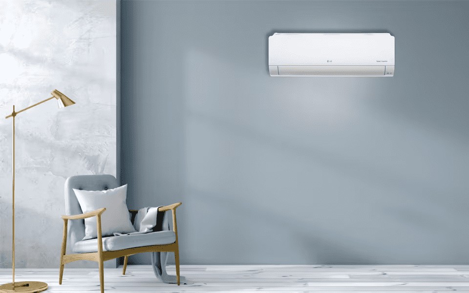مكيف هواء LG DualCool أبيض أنيق على جدار أزرق فاتح في غرفة حديثة بها كرسي بذراعين رمادي ومصباح ذهبي.