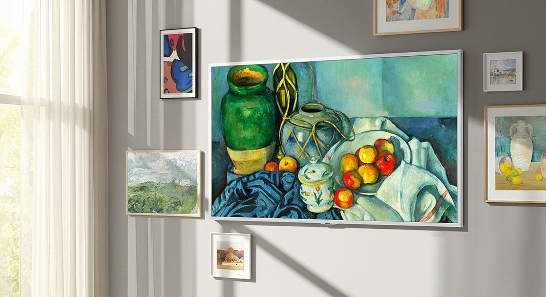 تلفزيون LG Gallery AI مع إطار LX7 ART TV يتميز بشاشة تشبه المعرض، مثبت على الحائط مع لوحة طبيعة صامتة معروضة. إنه موضوع بالقرب من نافذة مع أعمال فنية أخرى مؤطرة، وعلى الرغم من ضوء الشمس، لا تظهر على شاشته أي انعكاسات مرئية، مما يجعله يبدو كعمل فني حقيقي.