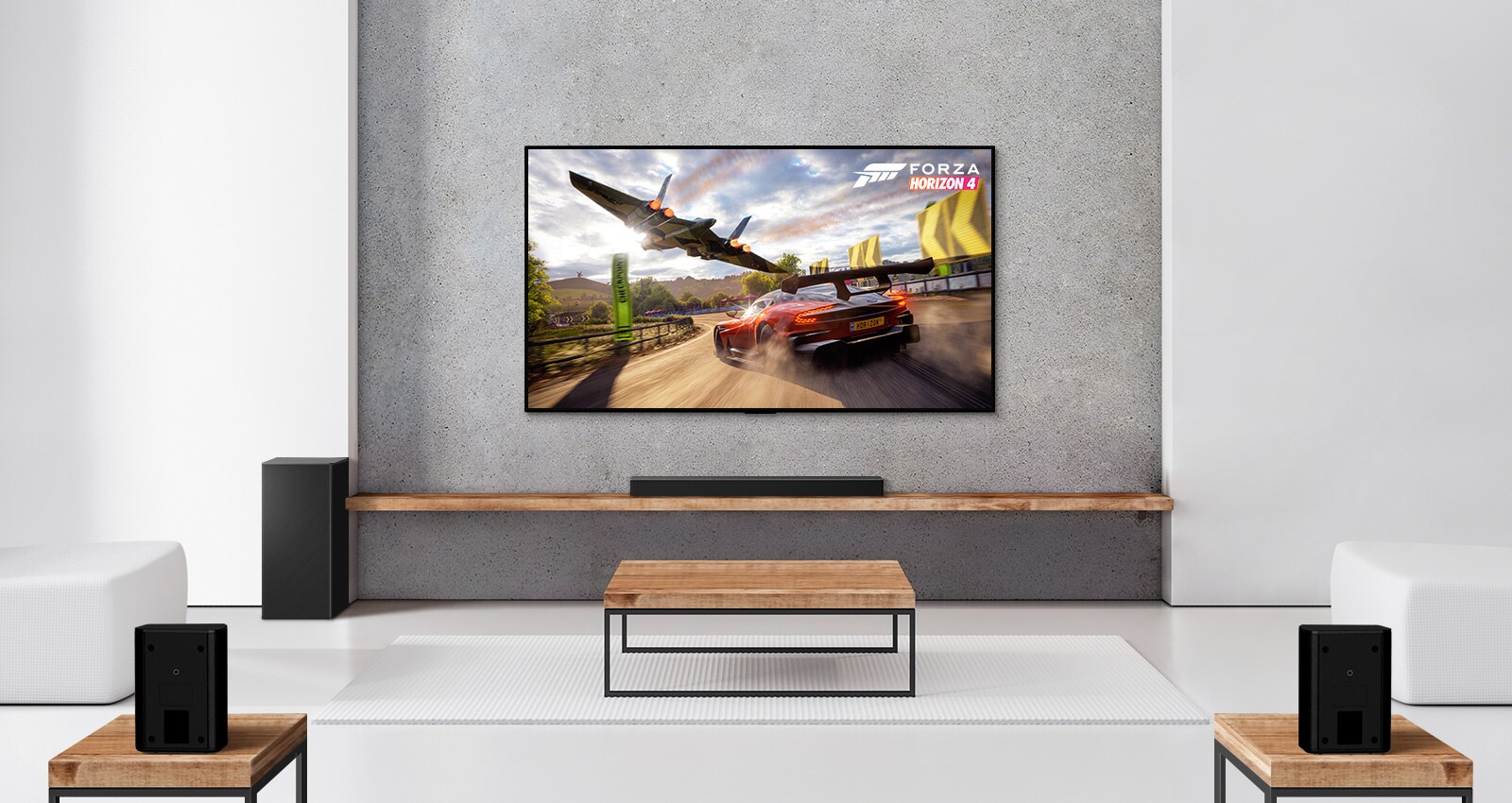 A set of 2 rear speakers, subwoofer, and a soundbar, and TV are in a white living room. A driving car and a spaceship are on TV screen. 