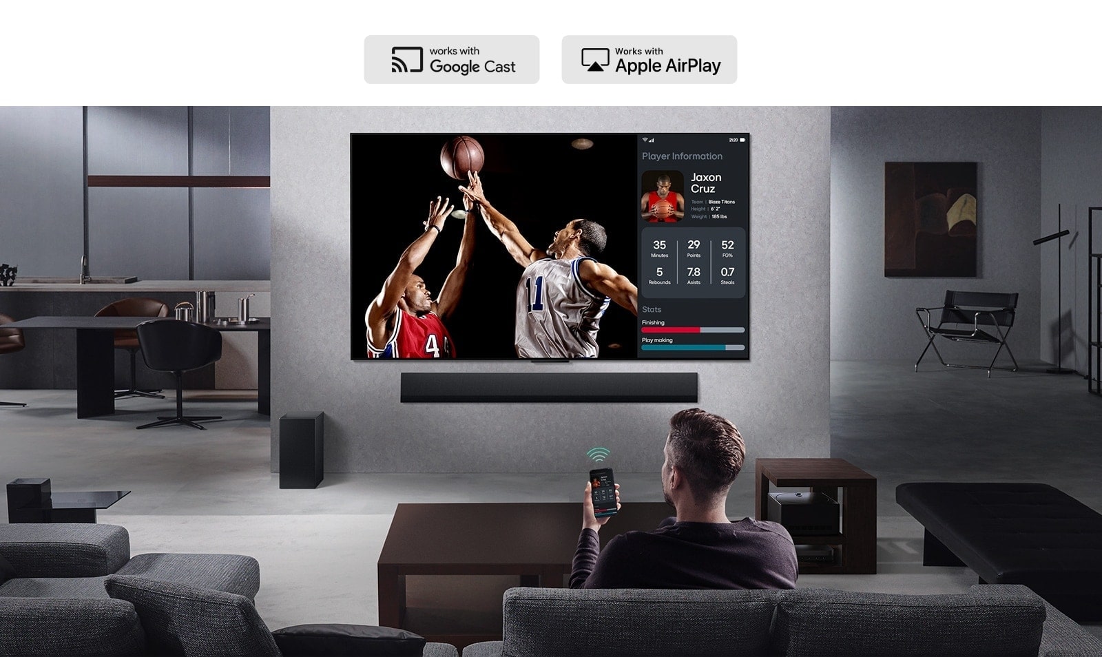 Person in their living room holding their phone. On the phone is a transmitting icon showing that the phone screen is being mirrored on the TV. On the TV is a basketball game to the side is the mirrored screen, showing player statistics. 