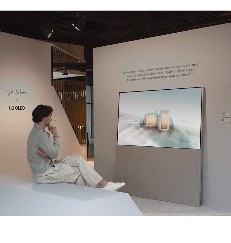 The image shows a person sitting on a chair looking at dreamlike scenery set among the clouds playing on Easel. On another wall, an LG OLED display shows an image of snow-covered trees reaching into the sky.