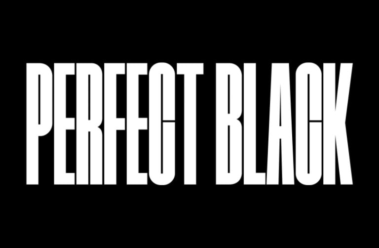 The words "PERFECT BLACK" appear in bold black capitals. A black mountainous scene with crisp definition then rises to cover the letters, also revealing a village and sand dunes. The black copy disappears behind a black sky.