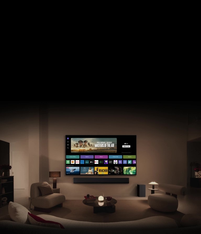 LG OLED TV showing the buttons Home Office, Game, and Music over a banner for Masters of the Air zooms out to show the TV mounted on a wall in a living room. The following logos are displayed on the TV screen in the image: LG Channels, Netflix, Prime Video, Disney TV, Apple TV, YouTube, Spotify, Twitch, GeForce Now and Udemy.