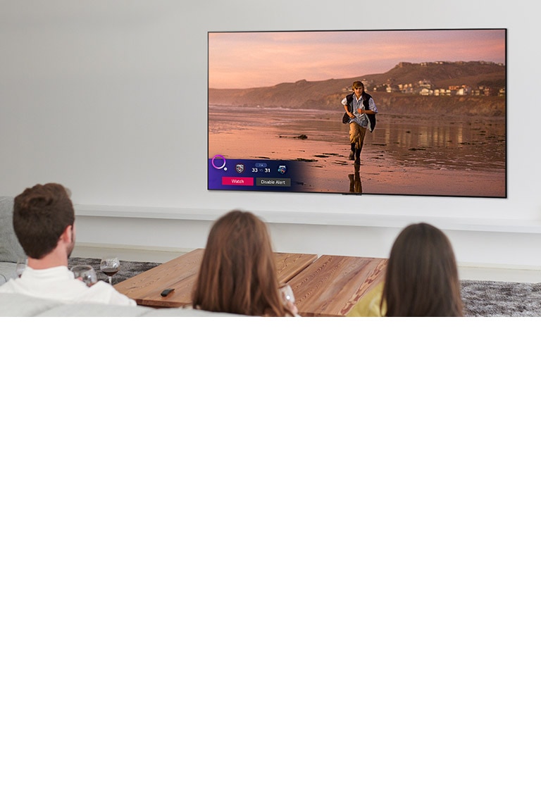 Three people watching TV screen showing a scene from a fantasy movie with a Sports Alert