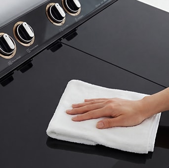 Hand wiping a black tempered glass washing machine lid, highlighting a scratch-resistant and easy-to-clean surface.
