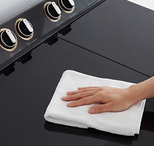 Hand wiping a black tempered glass washing machine lid, highlighting a scratch-resistant and easy-to-clean surface.
