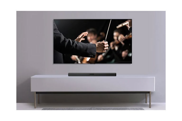 A TV is shown on a gray wall and LG Soundbar below it on a gray shelf. TV shows a conductor conducting an orchestra. 