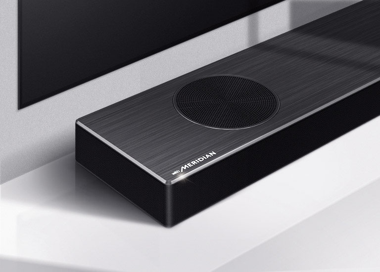 Close-up of LG Soundbar left side with Meridian logo shown on bottom left corner on a product. Bottom left side of TV is also visible. 