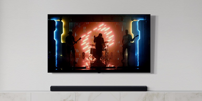 There is a TV and a soundbar in white living room. A group of band playing instruments and singing song on a TV screen. (play the video)
