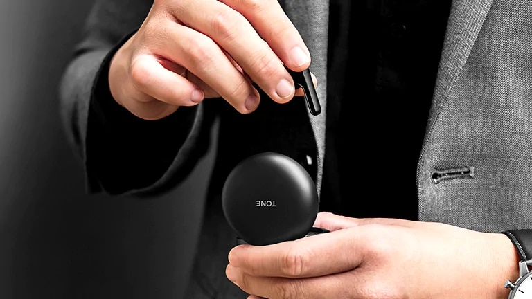 An image of a man dressed in grey suit holding a black LG TONE Free FN4 cradle and taking out an earbud from it 