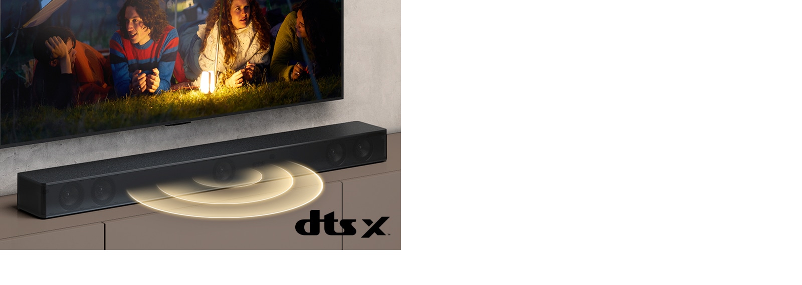 LG TV is on the wall, on the screen it shows 2 couples lying on the grass. In front of them, there is a lamp. LG Sound bar is below LG TV. Sound graphic is coming out from the front of the sound bar. DTS Virtual:X logo is shown on the bottom right corner of image.