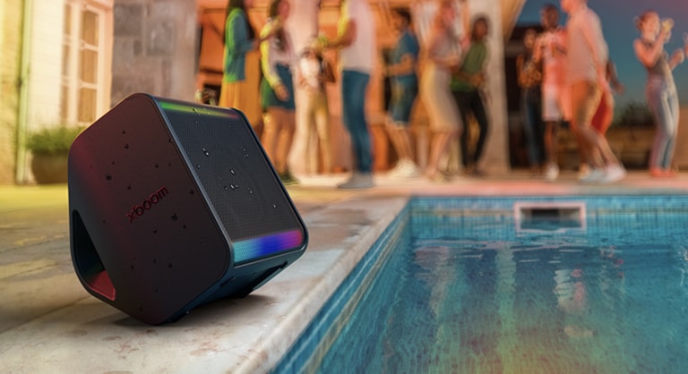 A sde of outddoor pool is shown and a flock of people is standing behind. xboom Stage 301 is placed facing to the pool with some splash of water on it.