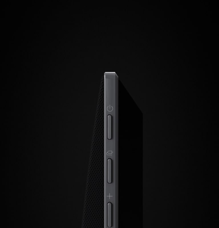 LG Soundbar is against a black backdrop opens to show the soundbar's side buttons, pans out, rotates to reveal its full design. The black backdrop transitions into a wall with an LG TV, and the soundbar mounts against the wall. 	