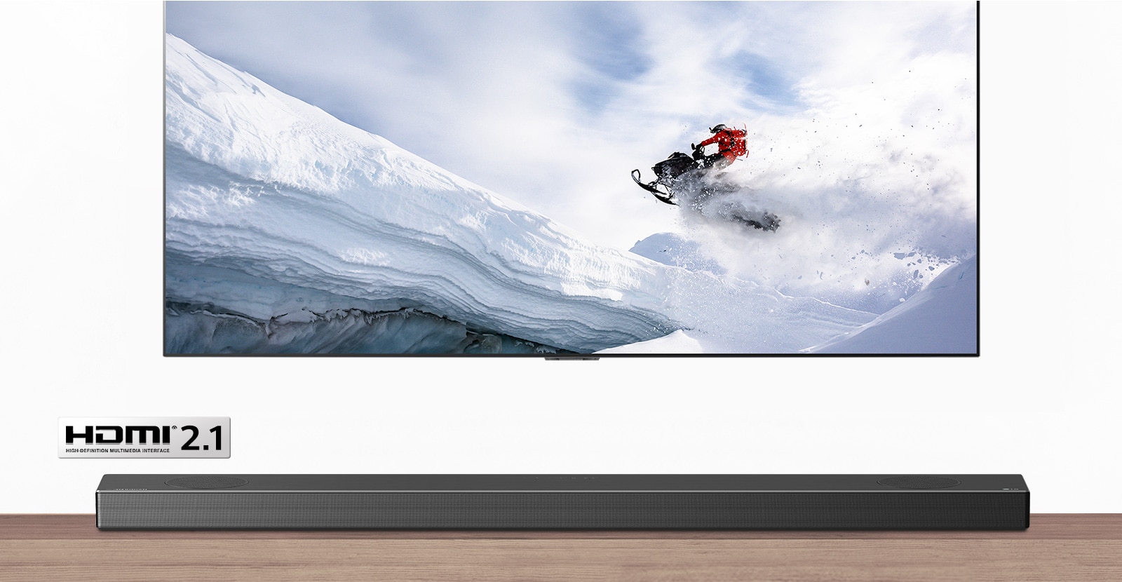 TV and Soundbar are seen from the front. TV shows man riding snowmobile in the snowy mountains. HDMI 2.1 logo is below TV. 