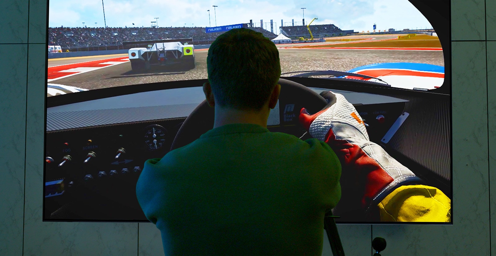 A man is sitting in a racing seat in front of a large TV playing a racing game.