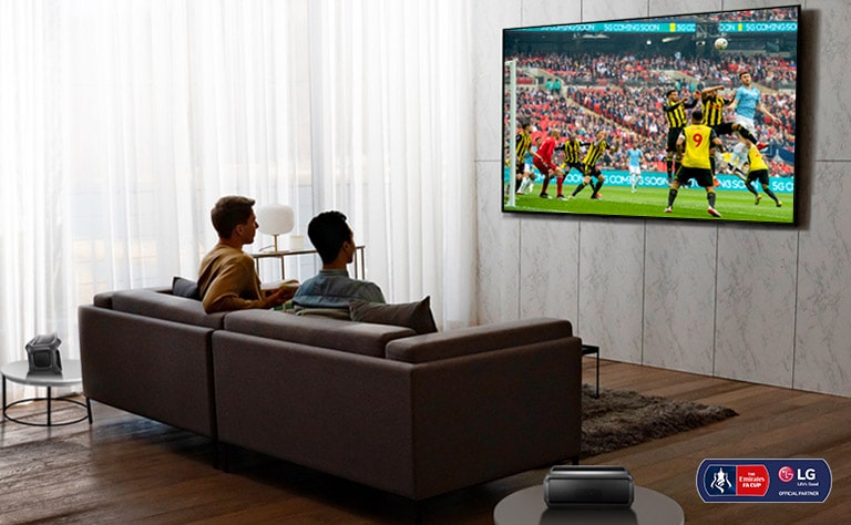 Two men are watching a sports game on TV in the living room with Bluetooth rear speakers.