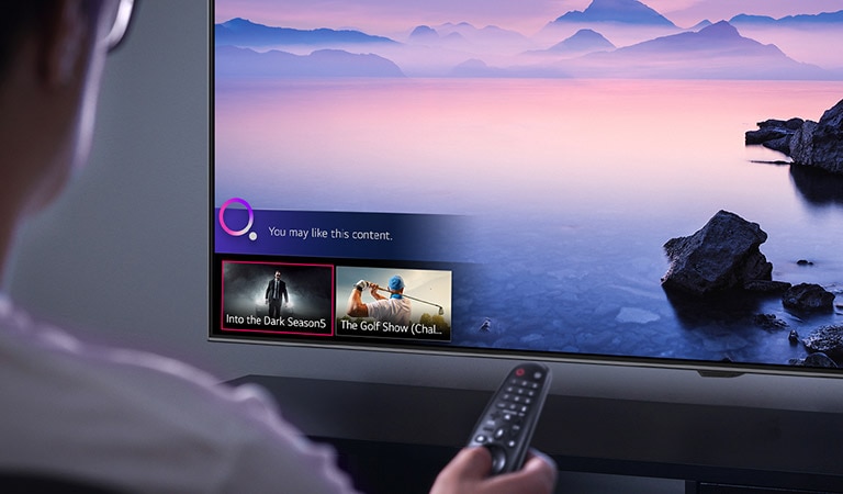 Closeup of a man choosing what to watch on TV with a remote control, with TV showing landscape.