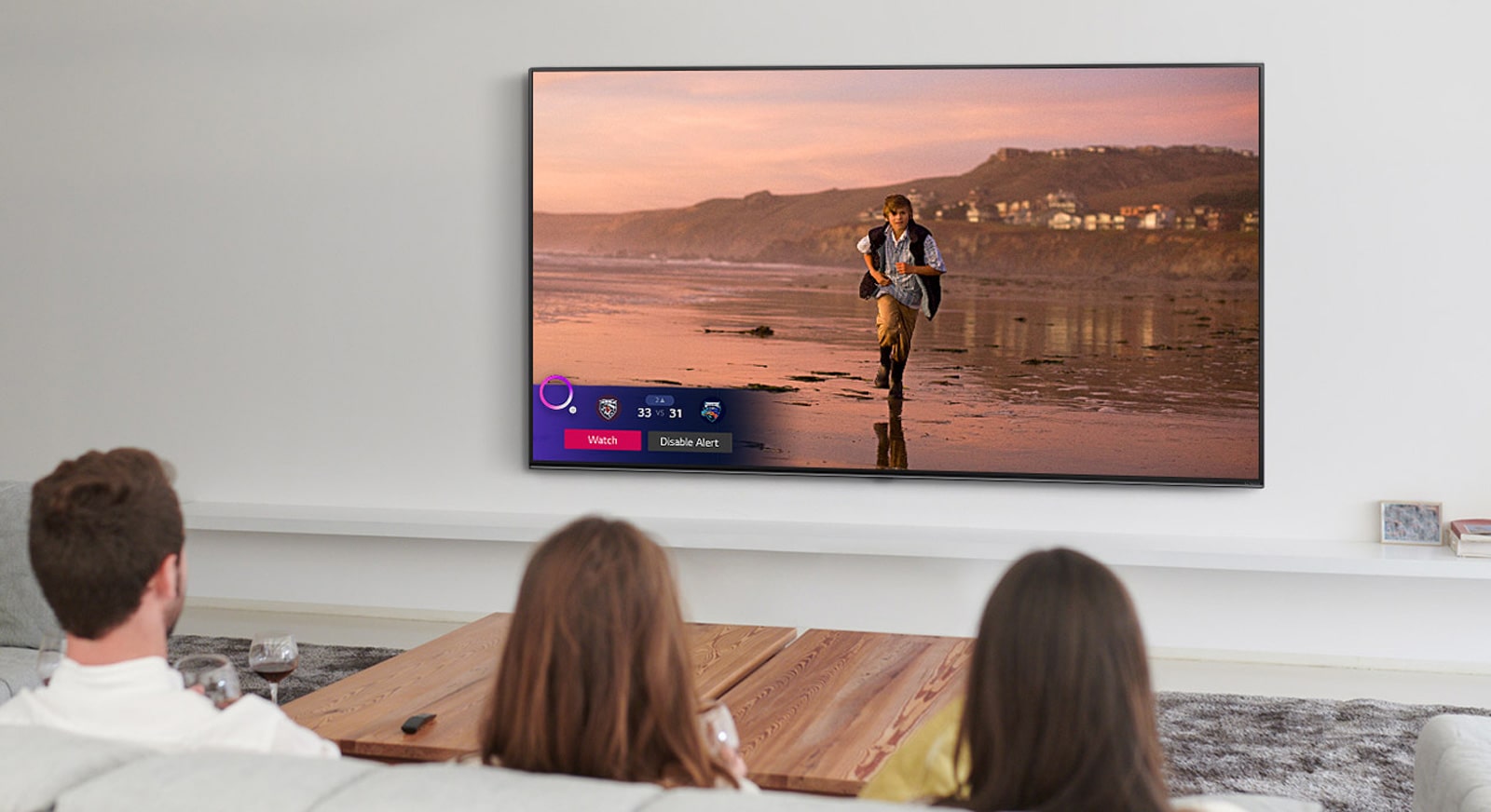 Three people watching TV screen showing a scene from a fantasy movie with a Sports Alert.