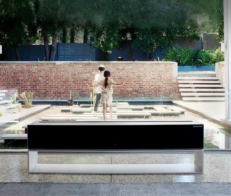 The screen of Rollable TV disappears in front of the pond in the luxury house, revealing the children playing behind