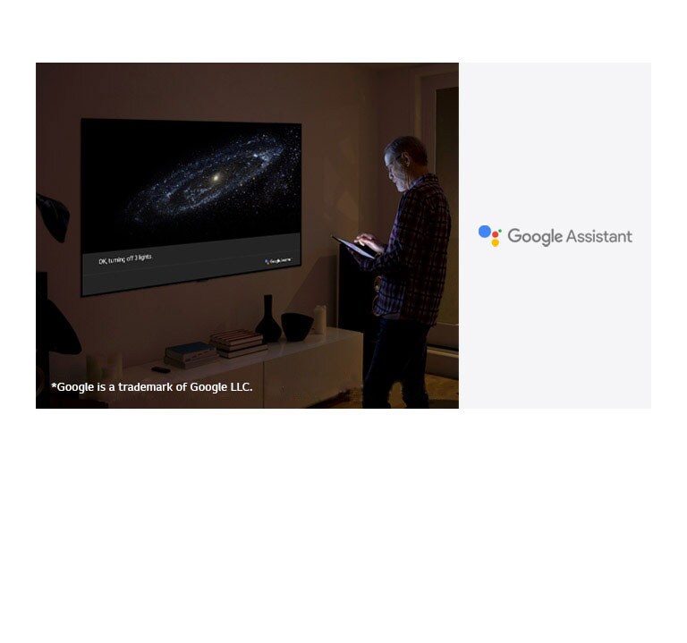 A man is standing in front of TV and ask google assistant to turn off the light