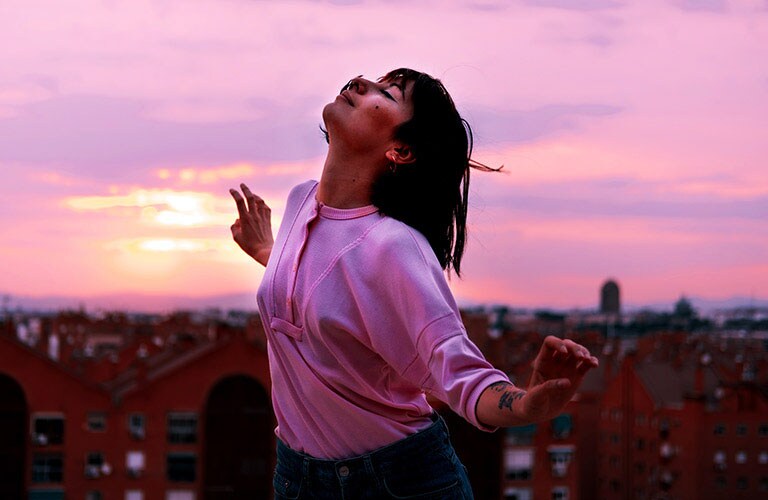 A bust shot of girl happily dancing on a roof at the magic hour