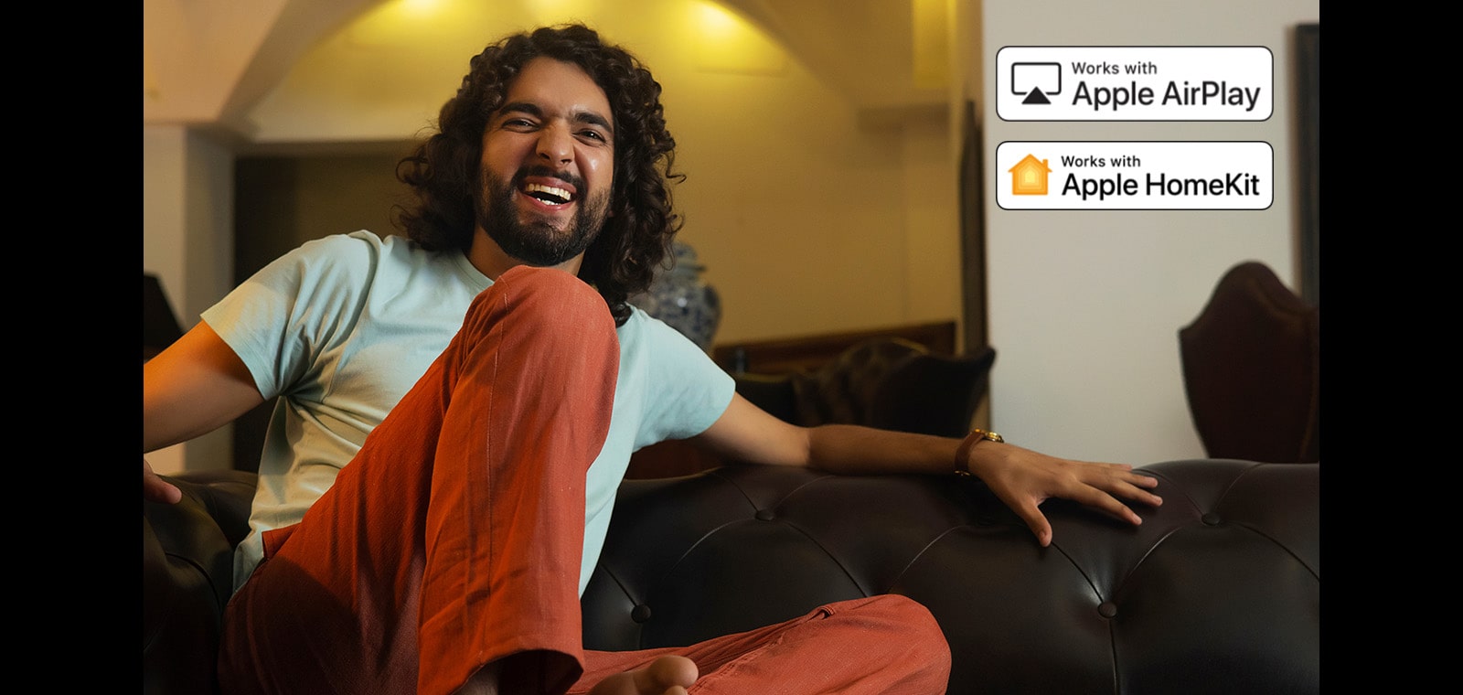 A man is watching something very happily. There is Apple AirPlay logo and Apple HomeKit logo on right top corner. 