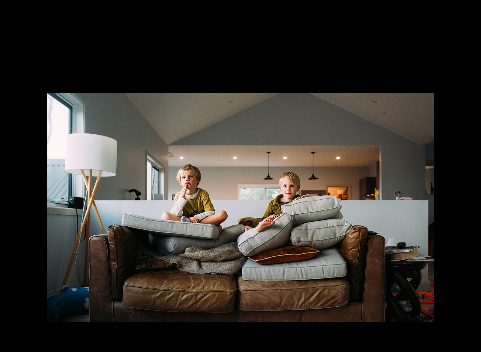 Two twin boys are watching something sitting on a sofa.