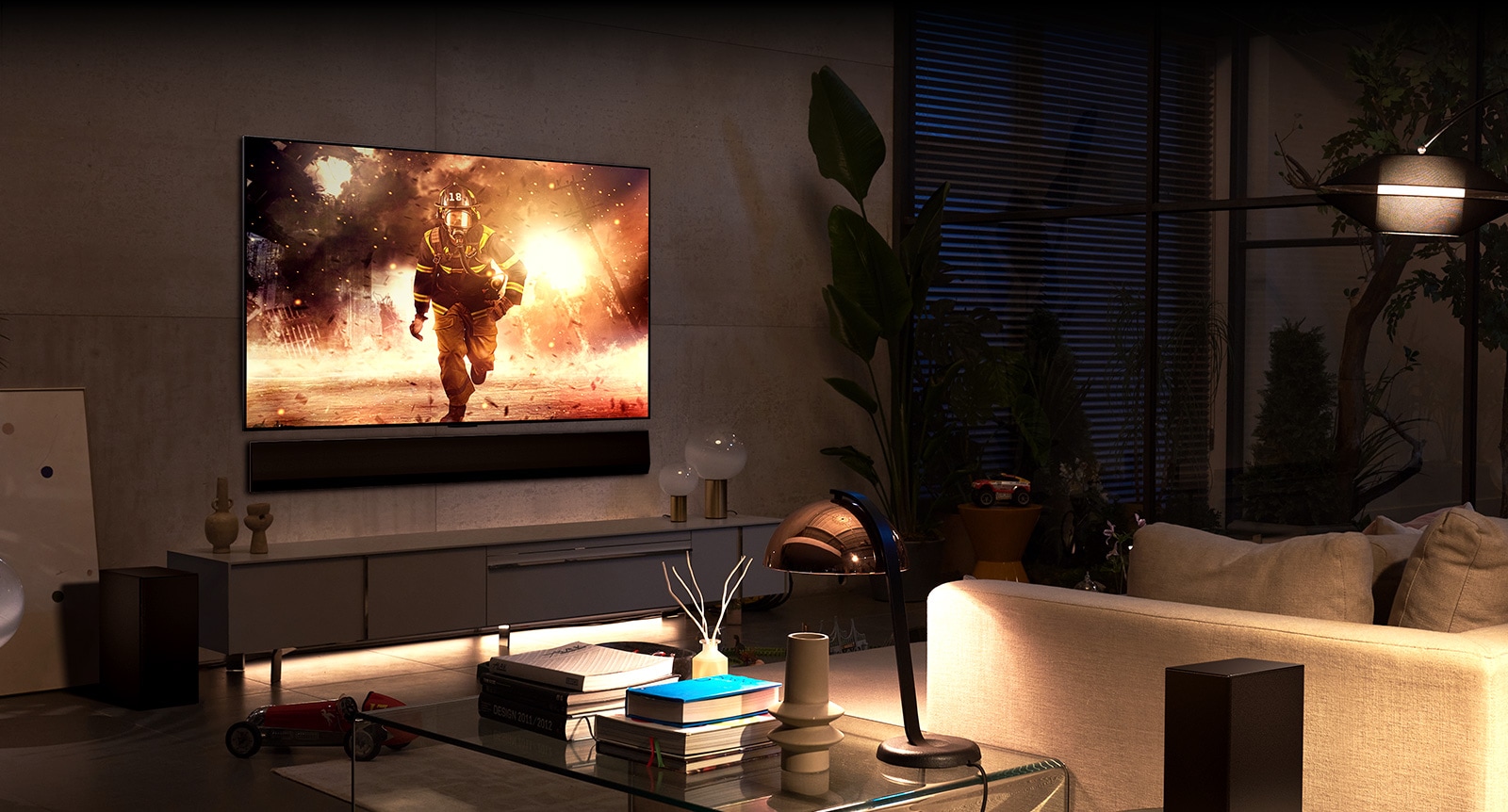 In a spacious and comfortable living room, a TV and soundbar are mounted on the wall. On the TV screen, a firefighter is seen jumping out of a burning building.