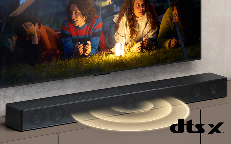 Le téléviseur LG est accroché au mur ; l’écran montre 2 couples allongés sur l’herbe. Devant eux se trouve une lampe. La barre de son LG se trouve sous le téléviseur LG. Un graphique représentant du son sort de l’avant de la barre de son. Le logo DTS Virtual:X est visible dans le coin inférieur droit de l’image.