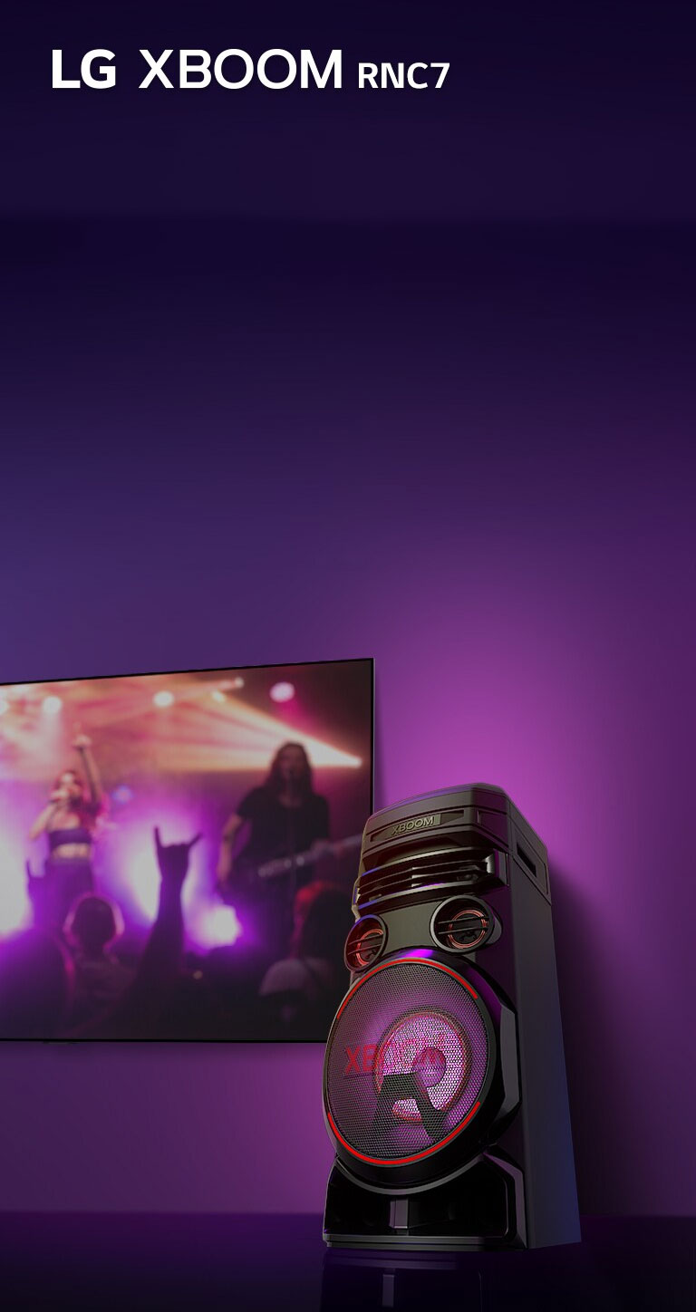 Vue en contreplongée du côté droit de l’enceinte LG XBOOM RNC7 sur fond violet. L’éclairage du XBOOM est également violet. Et un écran de télévision diffuse un concert.