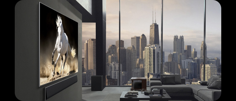 Appartement penthouse haut de gamme. L’horizon urbain est visible dans les baies vitrées du salon. La TV LG True Wireless et la LG Soundbar sont fixées au mur. Le design de l’espace est très sophistiqué et ordonné. Le boîtier Zero Connect est difficilement visible sous l’une des tables de chevet.